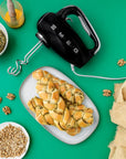 Black Smeg hand mixer on a green background with bread and ingredients
