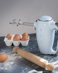 Pastel blue Smeg hand mixer next to baking materials on a black marble surface