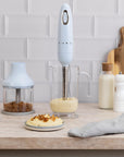 Smeg hand blender on a kitchen counter with various items including a cutting board and food.