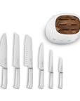 Top view of white Smeg knife block next to an assortment of knives lined in a row displayed on a white background