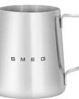 A SMEG branded stainless steel milk frothing jug with a handle and logo visible on the side.