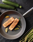 Salmon fillets in a pan with vegetables on a dark surface