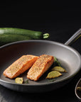 Salmon fillets in a frying pan with vegetables on a dark surface