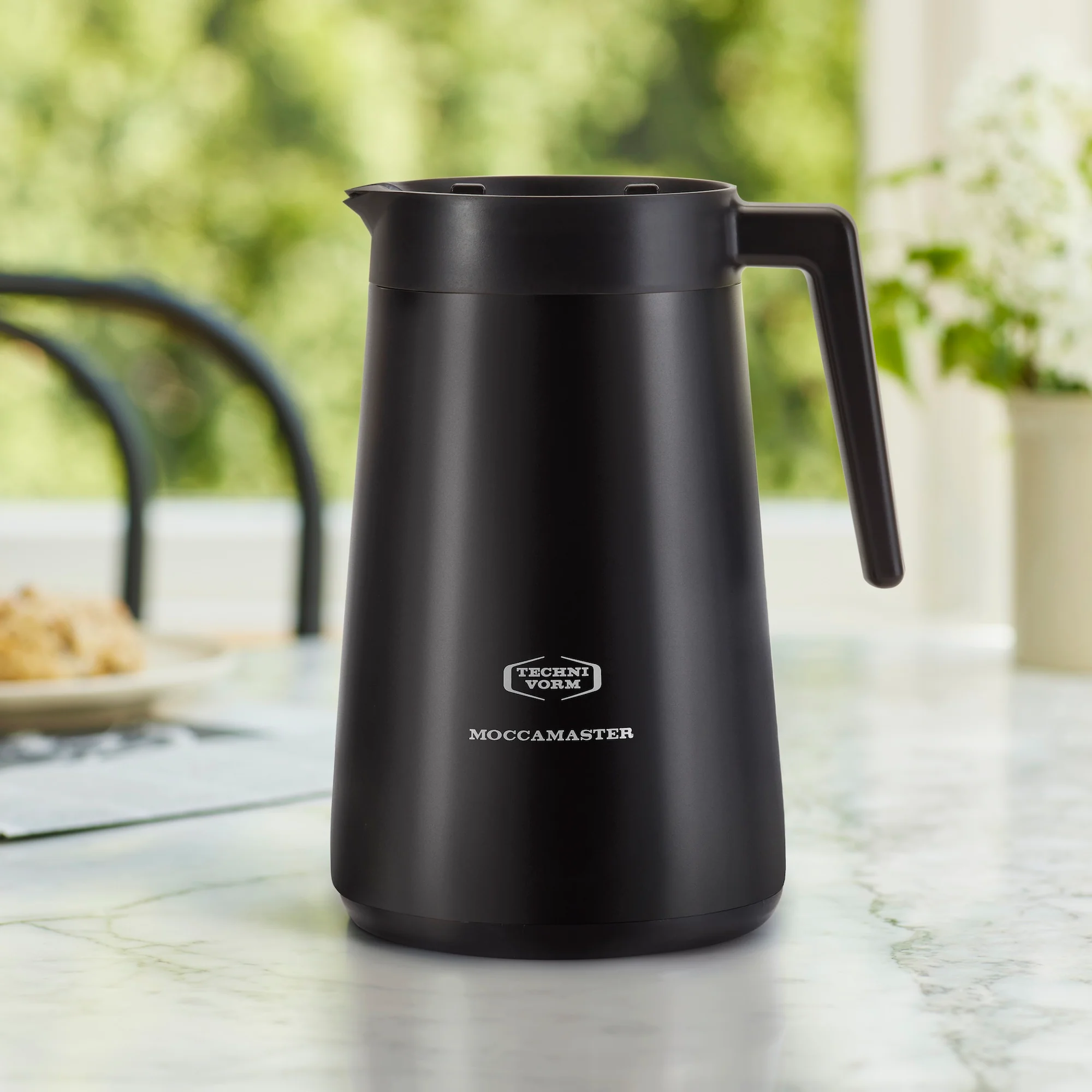 Black Moccamaster coffee pot on a table with a blurred outdoor background