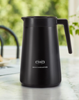 Black Moccamaster coffee pot on a table with a blurred outdoor background