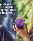Person holding a purple drink in a mason jar with a straw, outdoors.