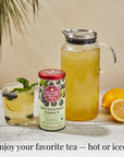 Blueberry Green tea next to glass of tea, jar of green tea, and lemons displayed on a white wooden surface