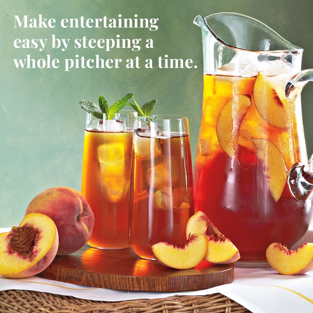 Peach iced tea with a pitcher and glasses on a wooden tray, surrounded by peaches.