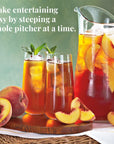 Peach iced tea with a pitcher and glasses on a wooden tray, surrounded by peaches.