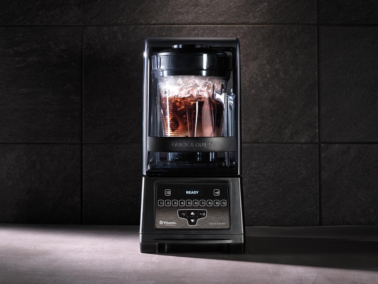 Blender with a glass container filled with a dark liquid on a dark tiled wall background