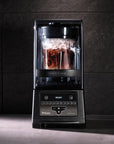 Blender with a glass container filled with a dark liquid on a dark tiled wall background
