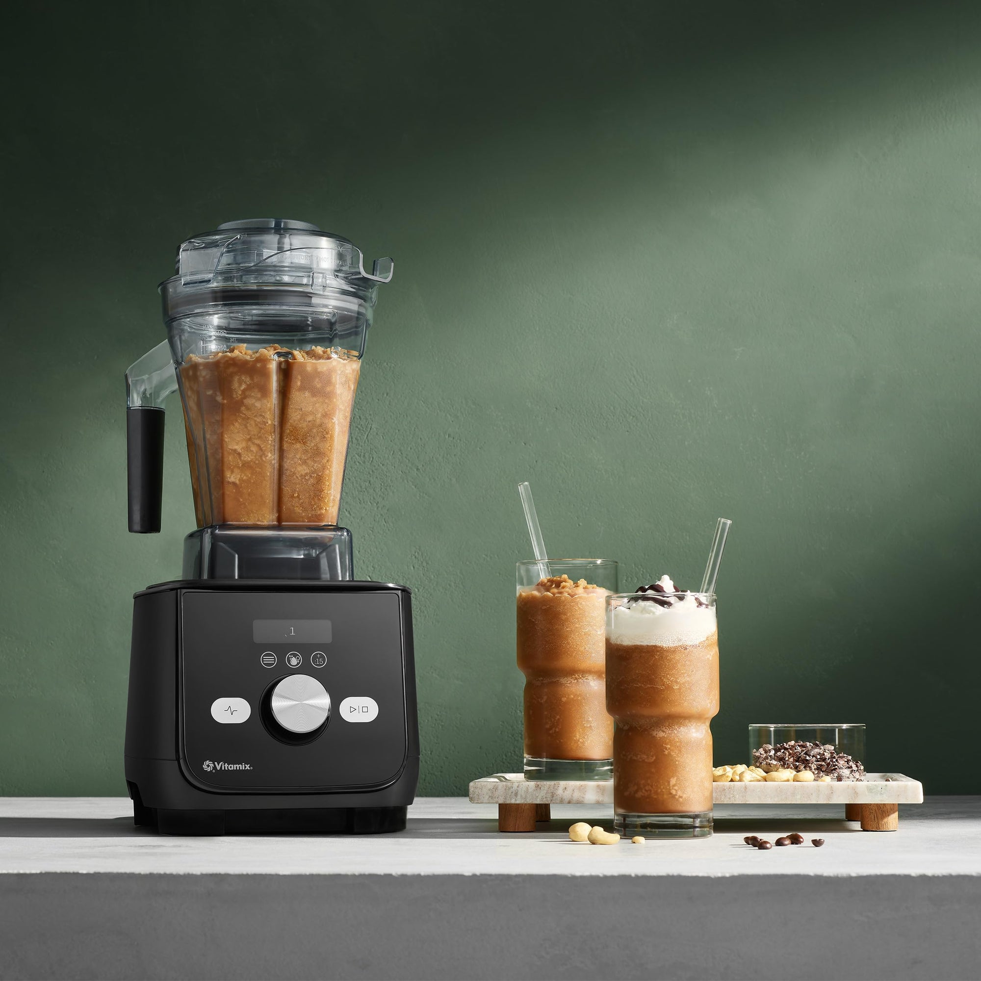 Black blender with a smoothie and ingredients on a green background