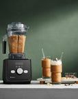 Black blender with a smoothie and ingredients on a green background