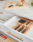 Open kitchen drawer with wooden knife block and cutting board on countertop