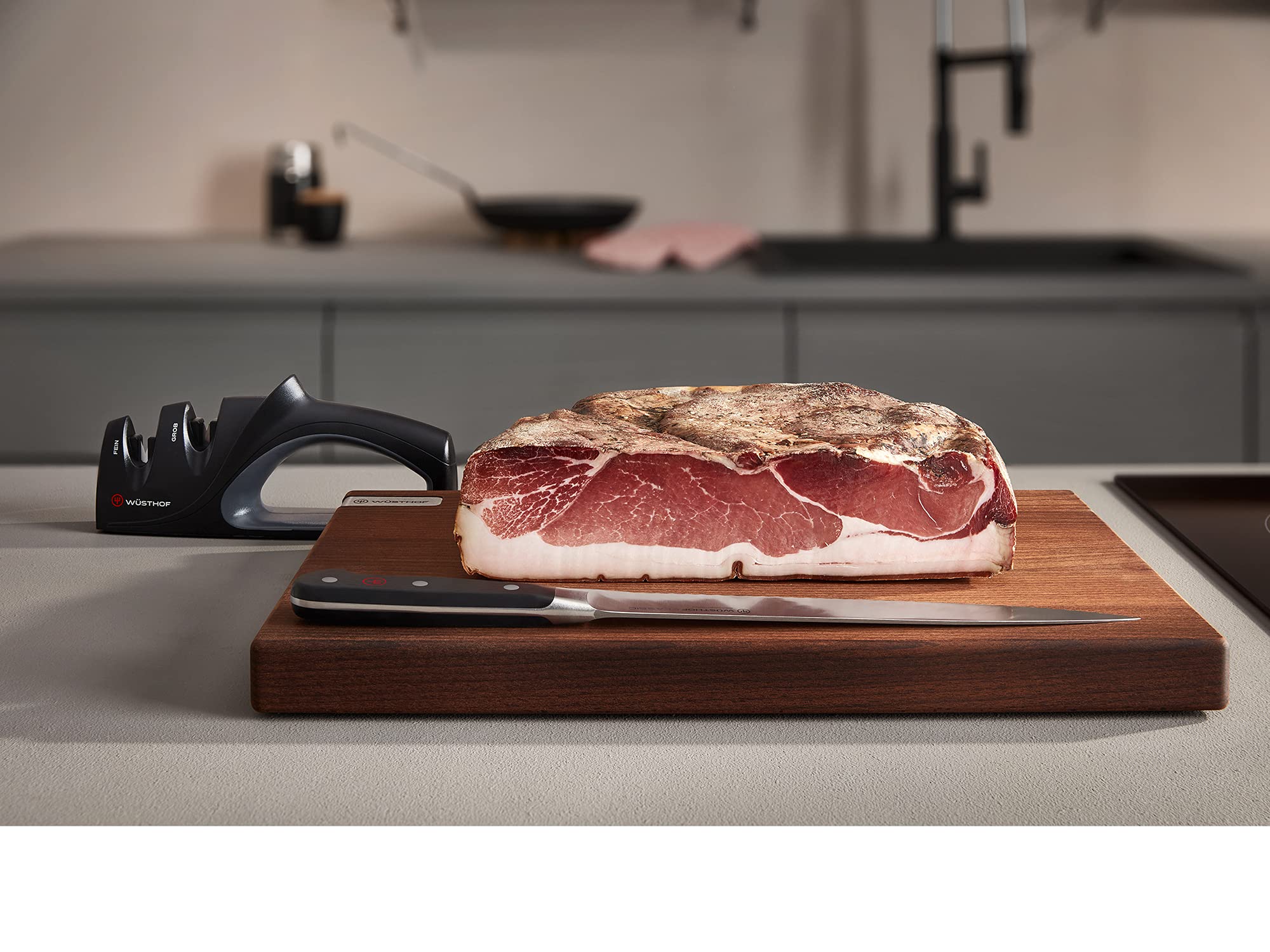 Raw meat on a cutting board with a knife and sharpener in a kitchen setting