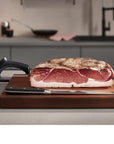 Raw meat on a cutting board with a knife and sharpener in a kitchen setting