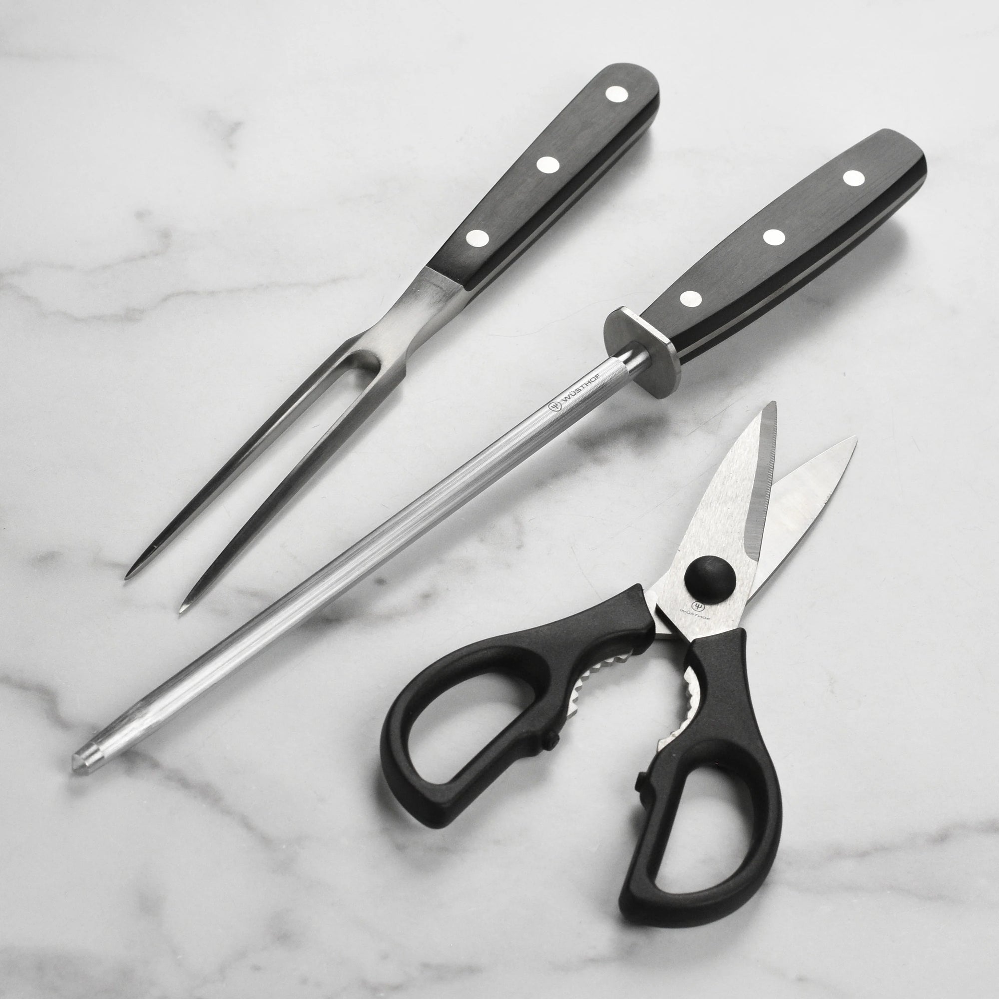 Set of kitchen utensils including a fork, knife, and scissors on a marble surface