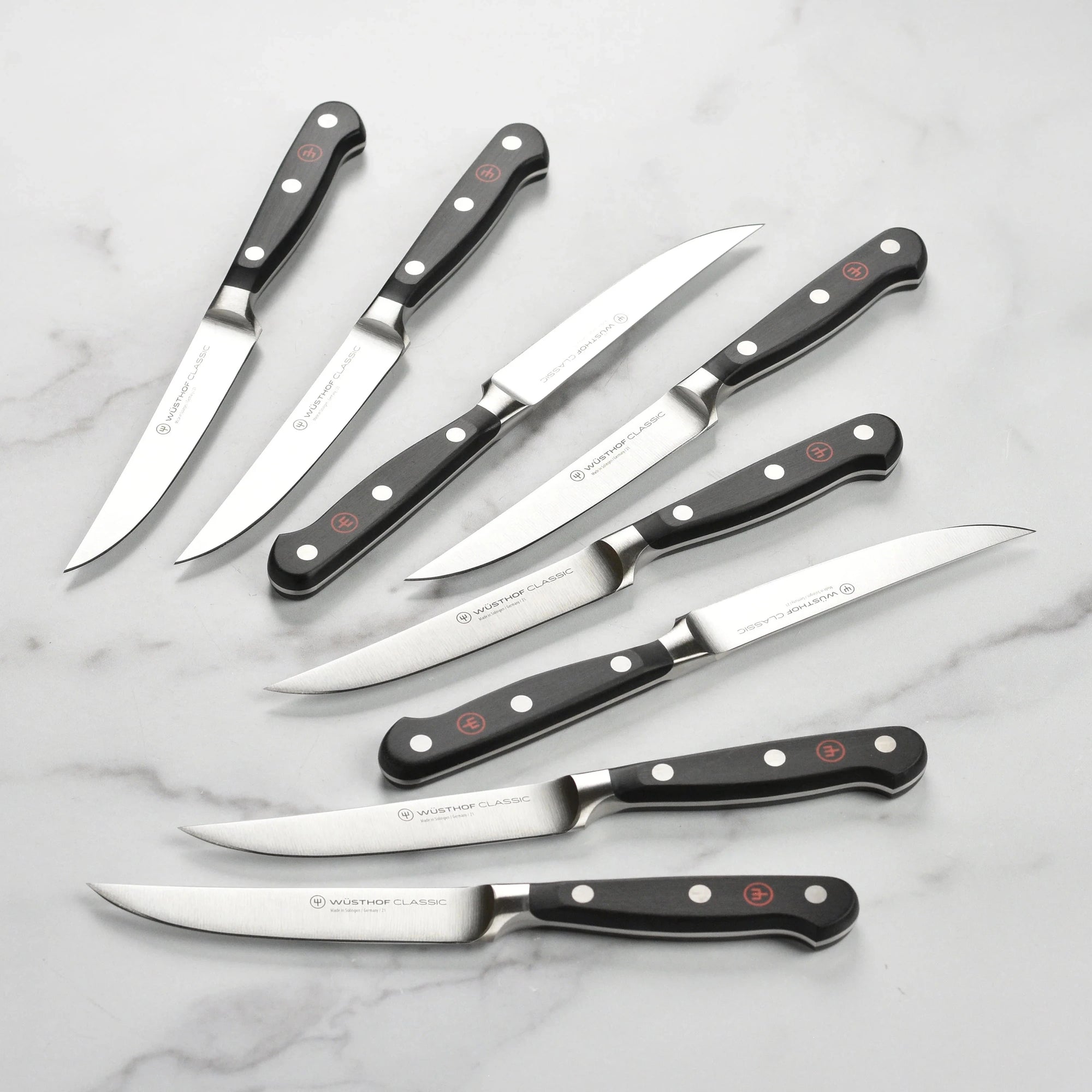 Set of seven steak knives with black handles on a marble surface