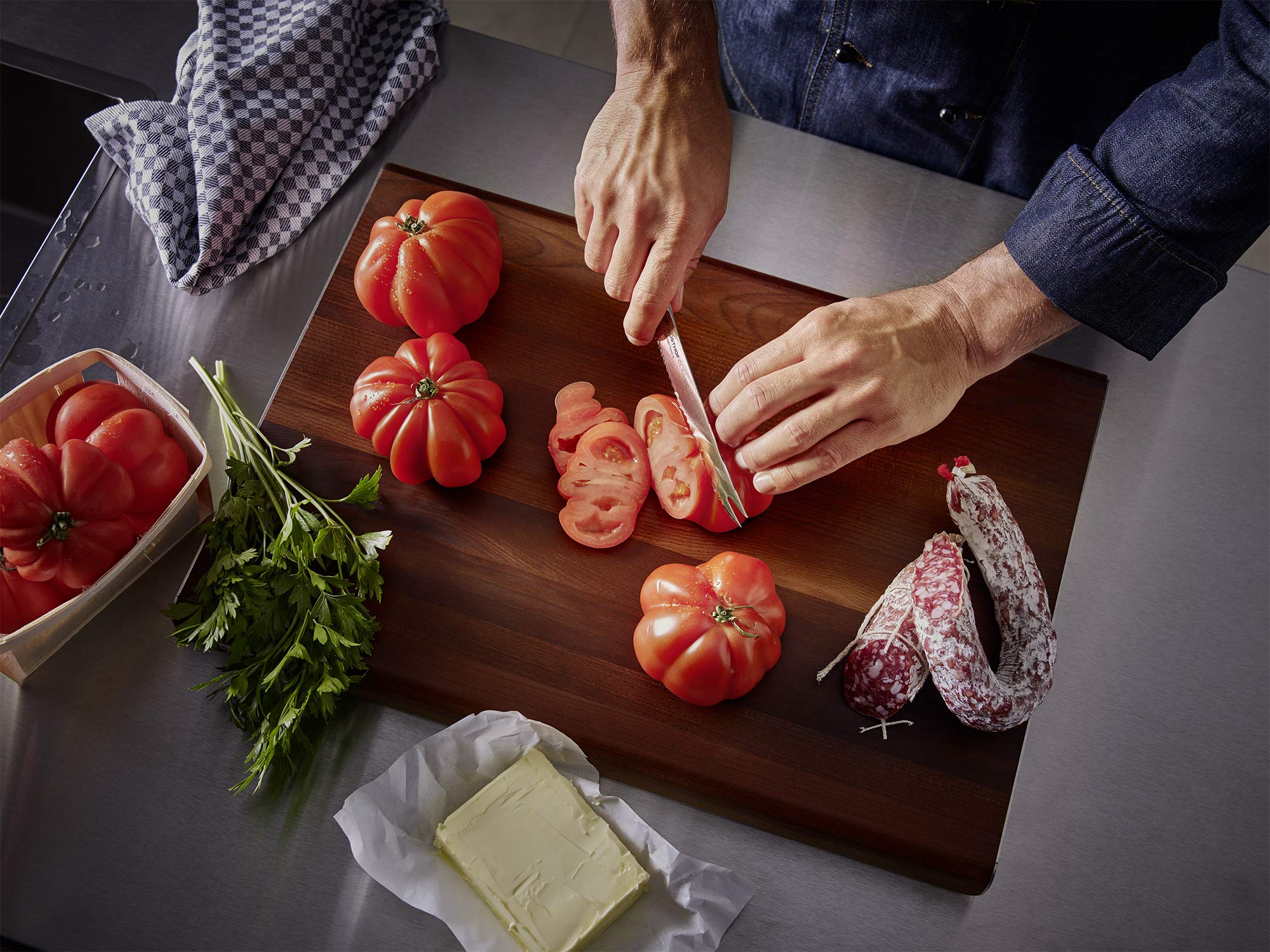 Person slicing tomatoes on a wooden cutting board with various ingredients around.