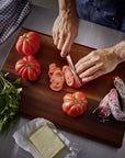 Person slicing tomatoes on a wooden cutting board with various ingredients around.