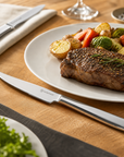 Steak with vegetables on a plate with a Wüsthof knife on a wooden table.